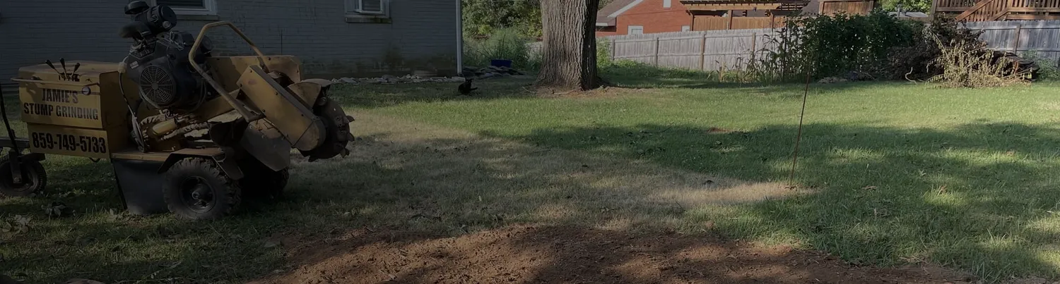 Yellow stump grinder sitting on a wide green lawn after grinding a stump, by Jamie's Stump Grinding in Harrodsburg KY